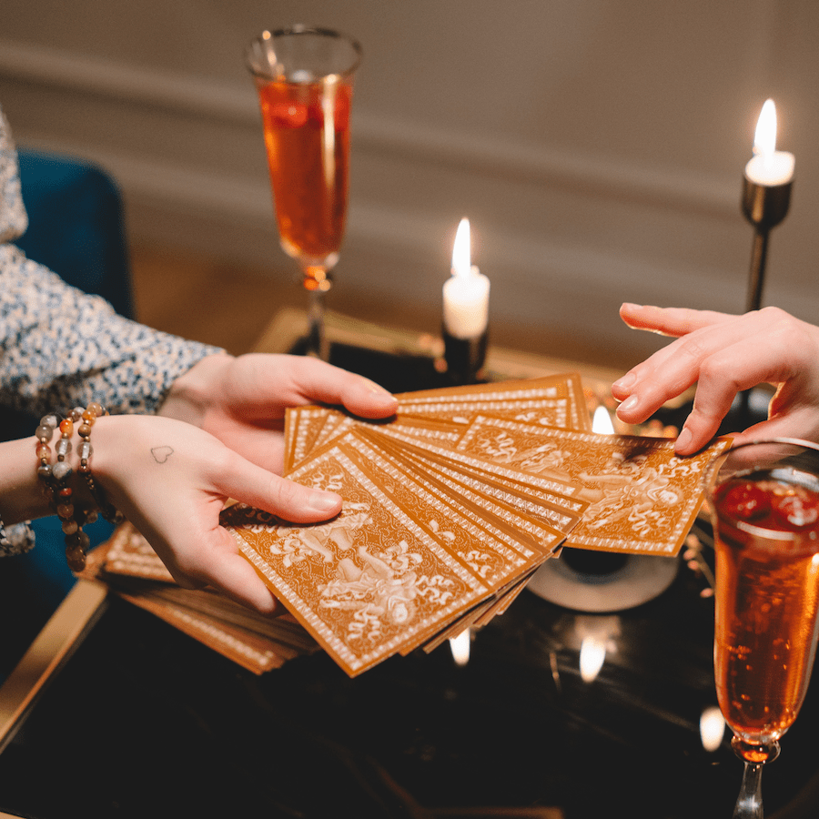 Two hands exchanging tarot cards over a candlelit table with warm amber lighting, creating a mystical and intimate atmosphere